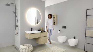 Un hombre camina en un baño con lavabo, WC, bidé y muebles de la serie Geberit iCon