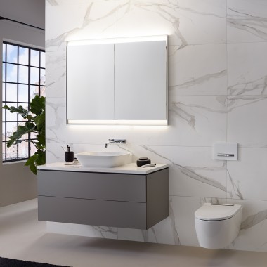Baño con pared con baldosas con aspecto de mármol, lavabo y mueble Geberit ONE y armario con espejo con luz ComfortLight